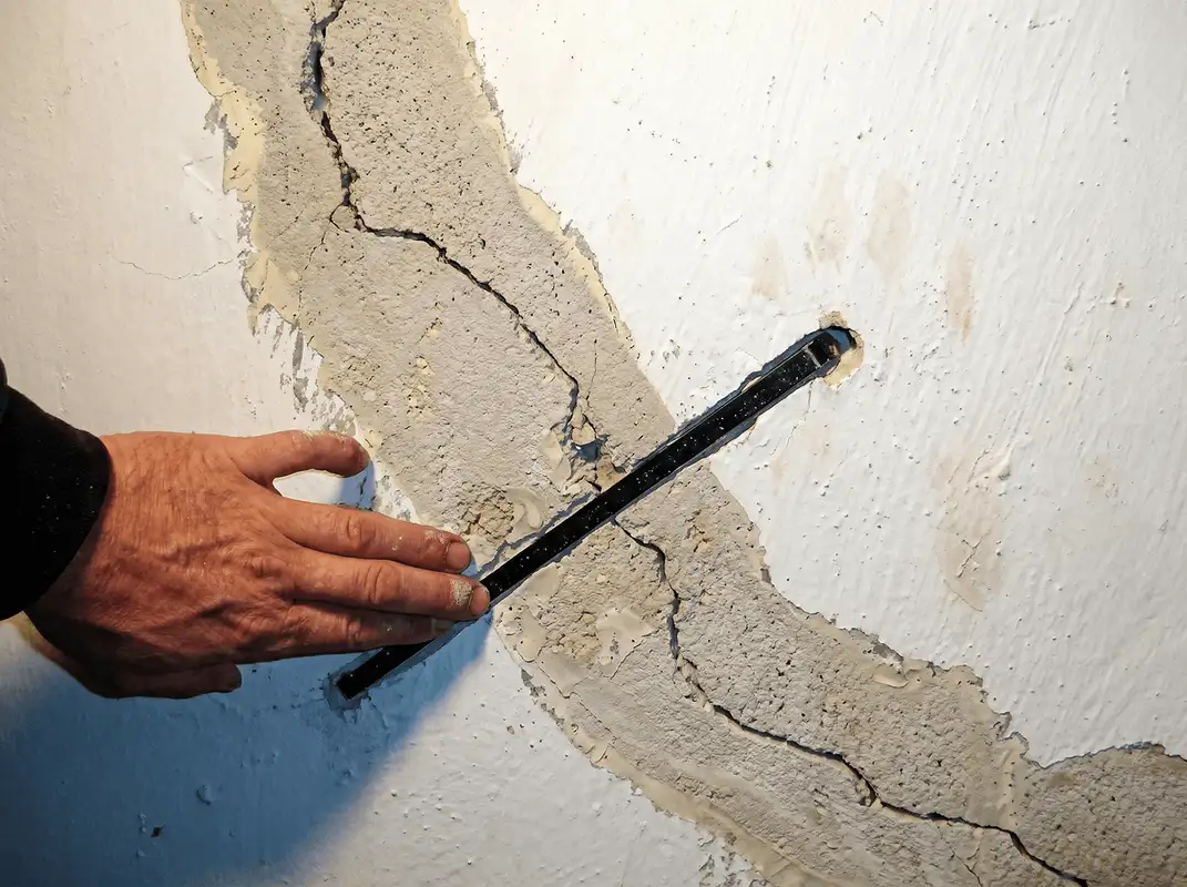 A wall with a large crack is being inspected by a professional in Charlotte, NC